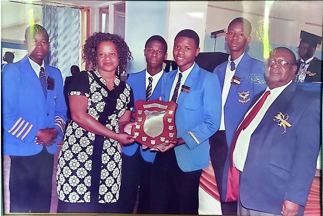 Students in blue blazers receiving a shield with staff
